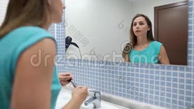 漂亮的女人在浴室镜子前用液体唇膏化妆嘴唇